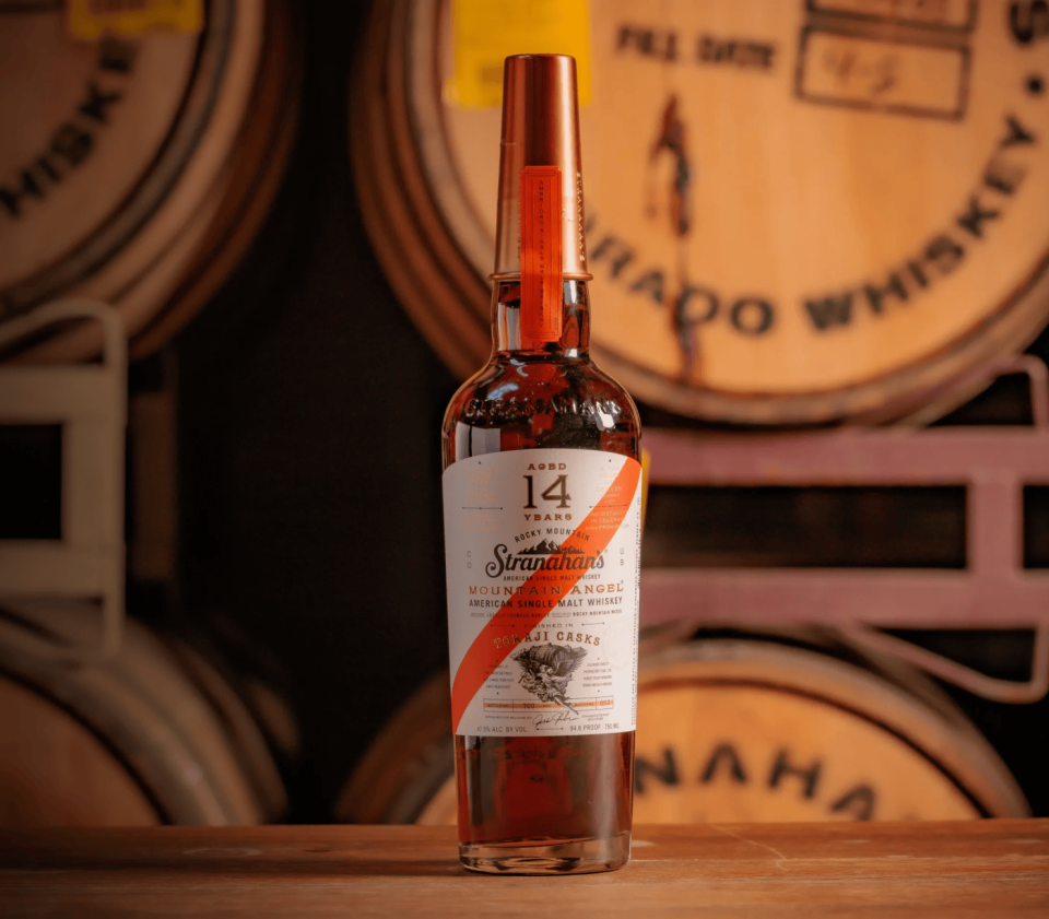 Stranahans Mountain Angel 14 Year bottle in front of whiskey barrels